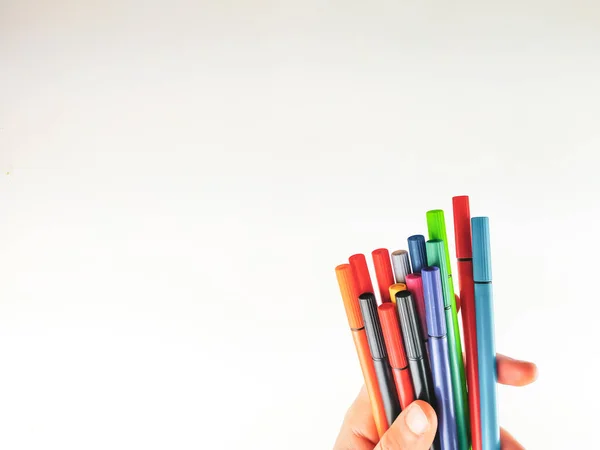 Primer plano y vista lateral de una mano sosteniendo muchos bolígrafos en diferentes colores sobre fondo blanco como lienzo en blanco para expresar imaginación y para la escuela — Foto de Stock