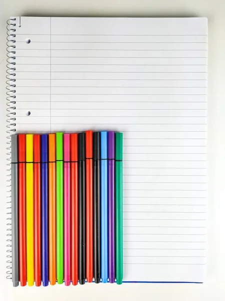 Back to school topic with top view of many pens in different colors placed on top of the notebook with lines, holes and spiral for good school year and studying — Stock Photo, Image