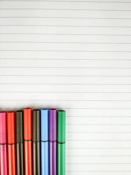 Muchos bolígrafos en diferentes colores con gorras en la esquina inferior alineadas en la parte superior del cuaderno blanco con líneas para tomar notas y una mejor organización en la escuela — Foto de Stock