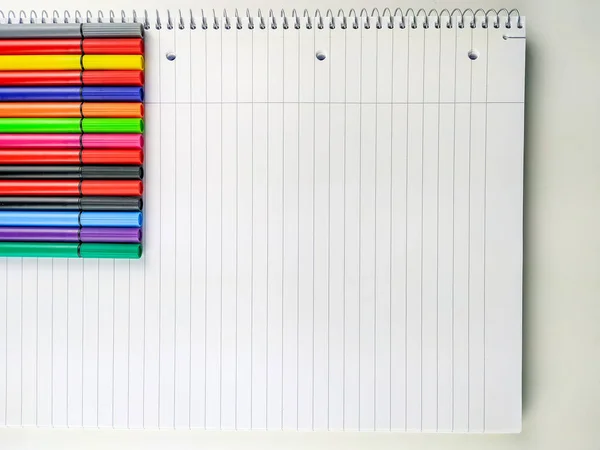 Mnoho barevných per s uzávěry na straně obrázku lemované na horní části bílého zápisníku s čarami pro psaní poznámek, kreslení a barvení — Stock fotografie