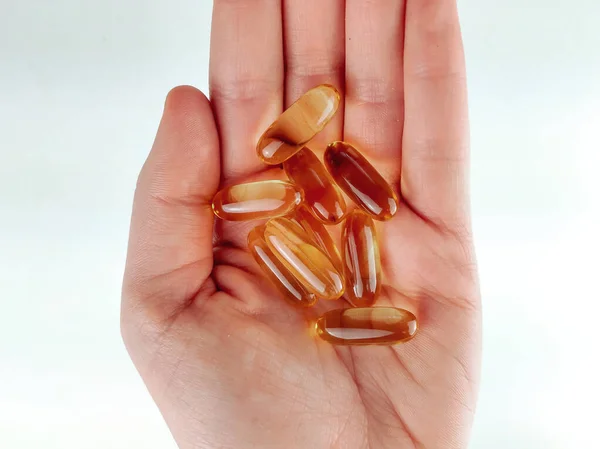 Top view closeup of a palm hand on white background holding handful of omega pills capsules as healthy cure, supplement and prevention