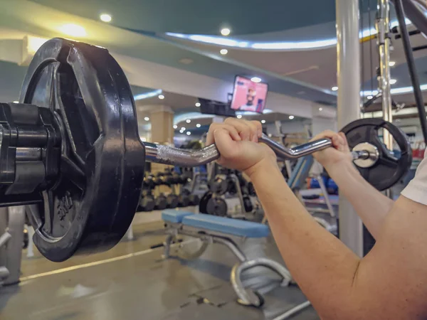 Άποψη ενός καυκάσιου νεαρού άνδρα χέρια άρση βάρους σε ένα σύγχρονο και καλά εξοπλισμένο γυμναστήριο για την αύξηση της δύναμης και της αντοχής και την απώλεια βάρους — Φωτογραφία Αρχείου