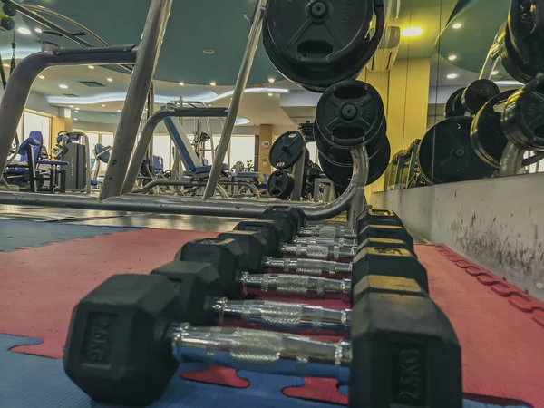 A lot of heavy dumbbells stacked and lined, organized on the soft rubber floor of modern gym interior with many different equipment in background for weight lifting and body building in retro style — Stock Photo, Image