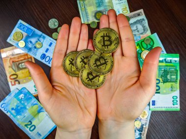 İki eliyle bir sürü altın bitcoin tutarak geleneksel para birimleri kağıt para ve metal madeni paralar arka planda bir seçim sunar