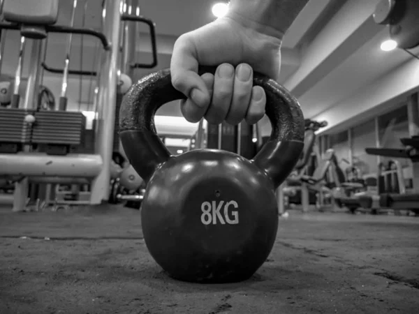 Αρσενικό χέρι μαζεύοντας ένα kettlebell ως στρογγυλή μπάλα σχήμα αλτήρα των 8 κιλών που τοποθετούνται στο εσωτερικό του δαπέδου γυμναστήριο για την απώλεια βάρους και bodybuilding σε μαύρο και άσπρο — Φωτογραφία Αρχείου