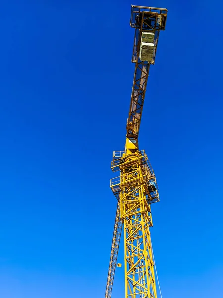 Hoge gele kraan gezien vanaf de grond met blauwe lucht op de achtergrond op de bouwplaats voor het bouwen en renoveren van architectuur — Stockfoto