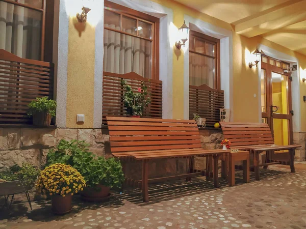 Όμορφος και ζεστός εξωτερικός σχεδιασμός με φυσική διακόσμηση και ξύλινα παγκάκια με κίτρινα φώτα το βράδυ και βραχώδες δάπεδο για την είσοδο του κτιρίου — Φωτογραφία Αρχείου
