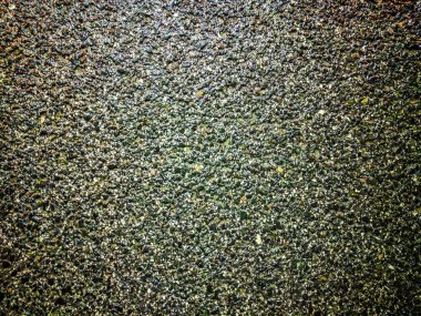 Islak asfalt beton yol, akşam saatlerinde şehir merkezindeki sokak lambalarıyla aydınlatılan küçük kaya taneciklerinin kaba dokusu.