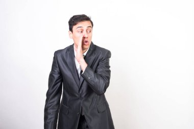 Takım elbiseli adam bir sır fısıldıyor, eliyle ağzını kapatıyor. Beyaz arkaplan, orta çekim