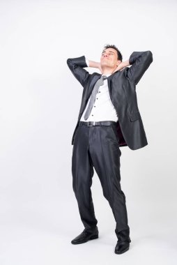 Takım elbiseli rahat bir adam elleri ensesinde geriye doğru eğiliyor beyaz arka plan, tüm vücudu.