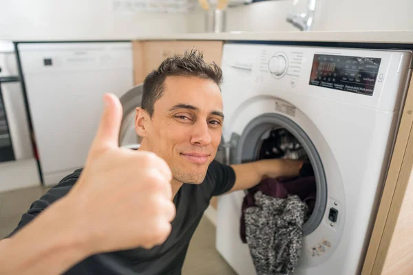 Mutfaktaki çamaşır makinesine çamaşır koyan gülümseyen adam. Kapat..