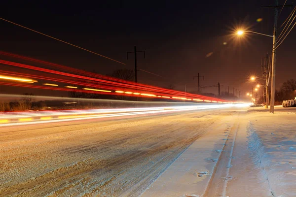 Schneebedeckte Winterstraße mit leuchtenden Straßenlaternen in ländlichen Gebieten bei Sonnenuntergang — Stockfoto