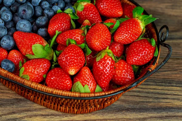 Fresas grandes de bayas rojas frescas en una canasta de mimbre sobre una mesa de madera — Foto de Stock