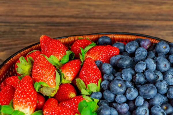 Mezcla de fresas frescas en una canasta sobre fondo rústico de madera — Foto de Stock