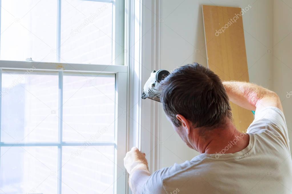 Carpenter using nail gun to moldings on windows, framing trim,