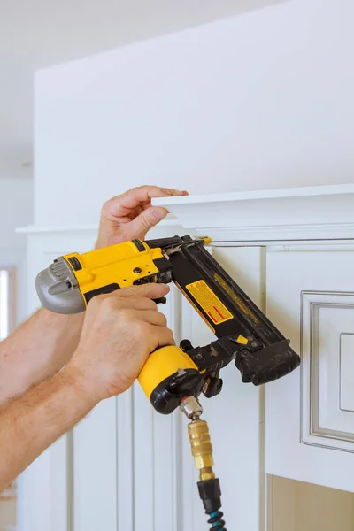 Carpenter brad using nail gun to Crown Moulding on kitchen cabinets framing trim, — Stock Photo, Image