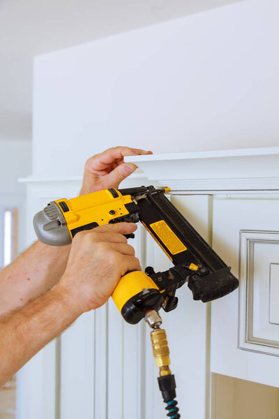 Carpenter brad using nail gun to Crown Moulding on kitchen cabinets framing trim,
