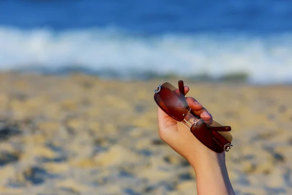 Frauenhand mit Sonnenbrille am tropischen Strand — Stockfoto