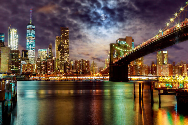 New York City's Brooklyn Bridge and Manhattan skyline illuminated at night with a full moon overhead.