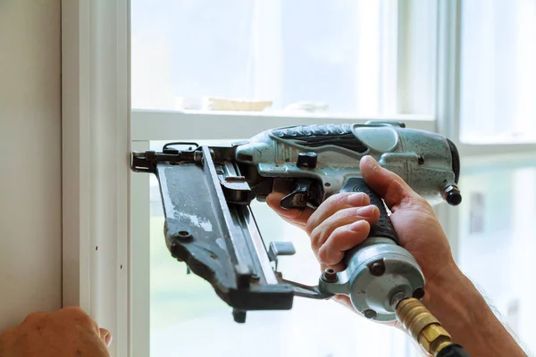 Carpenter brad using nail gun to moldings on windows, framing trim, — Stock Photo, Image