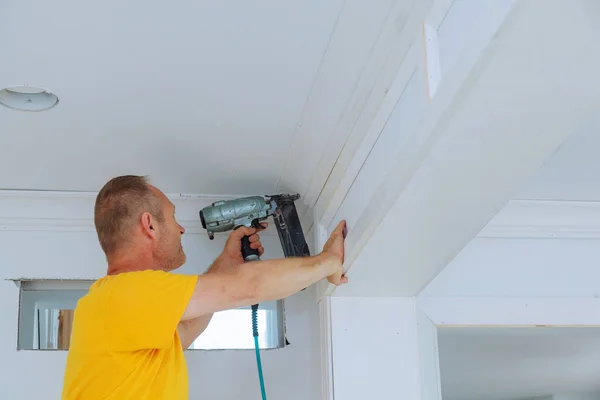 Carpenter brad using nail gun to Crown Moulding framing trim, with the warning label that all power tools — Stock Photo, Image