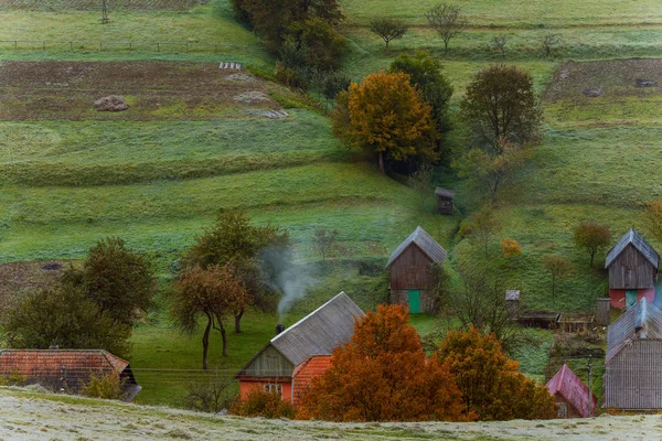 Pequena aldeia de montanha na colina com árvores coloridas verdes, alaranjadas e amarelas, campos, fundo das montanhas dos Cárpatos . — Fotografia de Stock