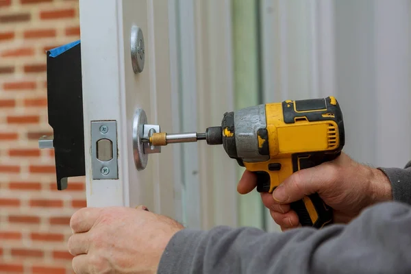 Instale la manija de la puerta con una cerradura, Carpintero apriete el tornillo, utilizando un destornillador de taladro eléctrico , —  Fotos de Stock