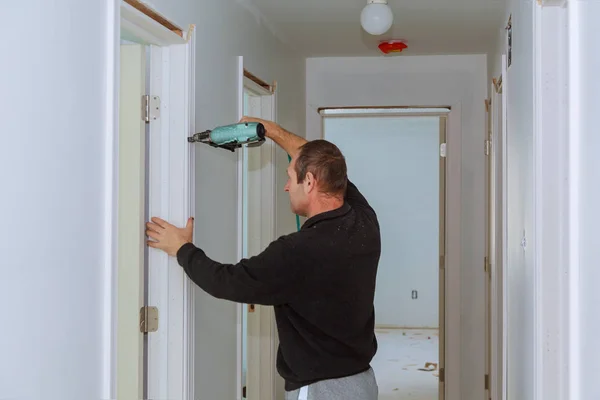 Carpinteiro brad usando pistola de prego para molduras em portas, moldando guarnição, com o rótulo de aviso de que todas as ferramentas elétricas — Fotografia de Stock