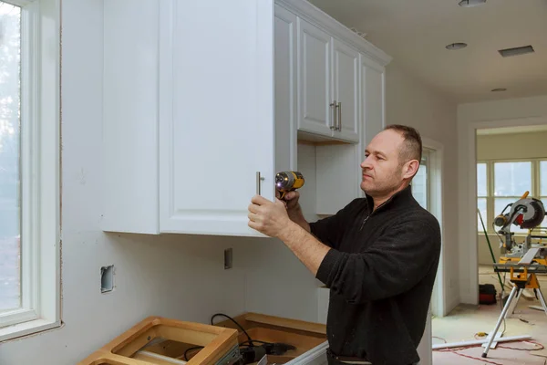 Trabalhador define uma nova alça no armário branco com uma chave de fenda instalando armários de cozinha — Fotografia de Stock