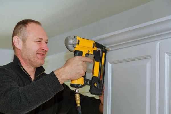 Carpenter using brad nail gun to Crown Moulding on kitchen cabinets framing trim,