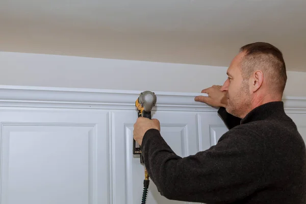 Handyman working using brad nail gun to Crown Moulding on white wall cabinets framing trim, Stock Picture