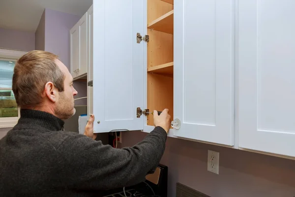 Munkavállaló állítja egy új fogantyú fehér szekrény egy csavarhúzóval telepítése konyha szekrények — Stock Fotó