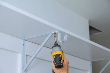 Arkadan görünüş iş gelen bir adamdır bir raf duvara yüklemek için bir matkap kullanarak