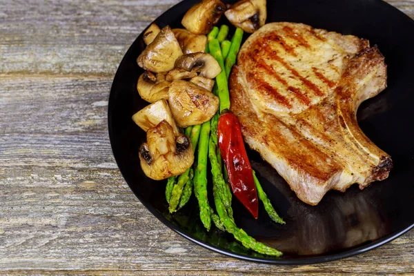 Izgara domuz biftek otlar, kuşkonmaz, mantar ile yakın çekim.