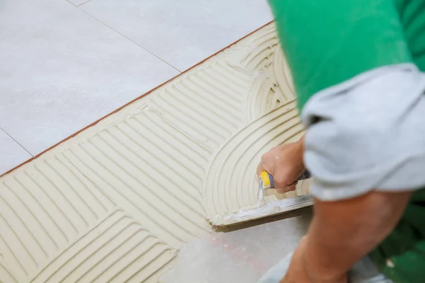 Operaio installa piastrelle sul pavimento. Ha messo colla con spatola pettine . — Foto Stock