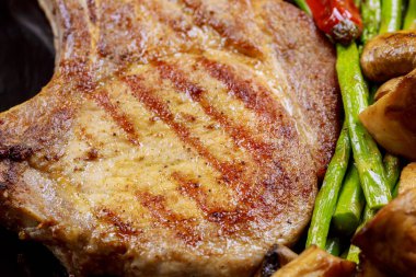 Izgara domuz biftek otlar, kuşkonmaz, mantar ile üzerinde ahşap arduvaz arka plan yakın kadar taş.