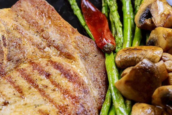 Gegrild varkensvlees biefstuk met kruiden, asperges, champignons steen leisteen achtergrond op houten dicht omhoog. — Stockfoto