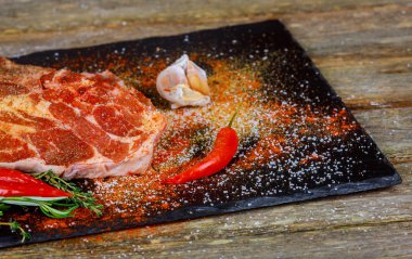 Siyah taş zemin üzerine baharat ile çiğ et biftek. Biftek yemek için hazır. Et kavurma için malzemeler.