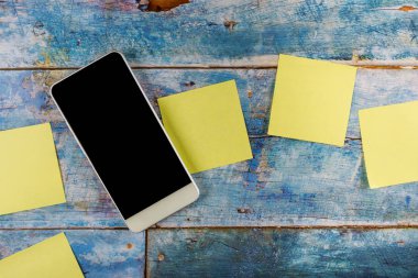 Sarı yapışkan notlar boş kare hatırlatıcı ile mavi ahşap arka planda akıllı telefon