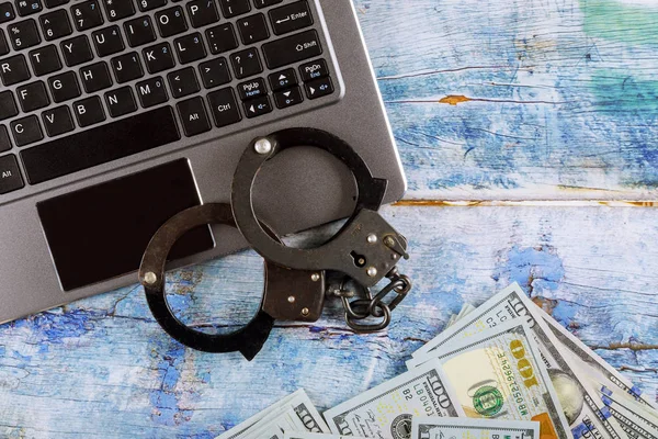 Steel police handcuffs on a pile of one hundred dollar bills with computer keyboard, technology cyber crime internet