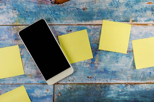Yellow sticky notes empty square reminder with smart phone in the blue old wooden background