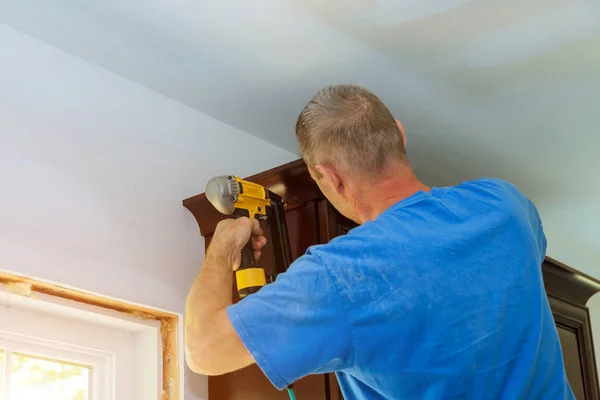 Trabajador de la construcción clavando pistola de aire de clavo brad para coronar el moldeo en gabinetes de cocina blancos —  Fotos de Stock