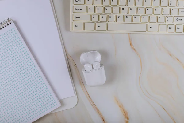 Bloc de notas en blanco sobre el teclado del ordenador y auriculares inalámbricos en la oficina en fondo de mármol — Foto de Stock