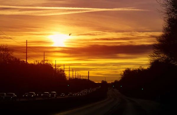 Estrada com carro após o pôr do sol brilhando os carros holofotes céu laranja — Fotografia de Stock