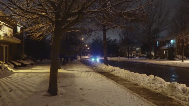 Carros dirigindo lentamente, neve coberta rua em uma área residencial à noite — Vídeo de Stock