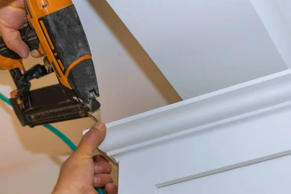 Carpintero de herramientas de clavador de aire que usa pistola de clavos para coronar molduras en gabinetes de cocina con gabinetes blancos — Foto de Stock