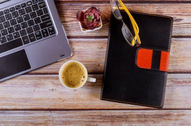 Düz masa masası çalışma alanı dizüstü bilgisayarı, klavyesi, not defteri, bardak ve kahve fincanı ahşap arka planda..