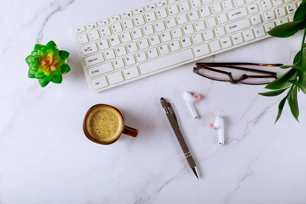 Mesa de escritorio de oficina con computadora suministros auriculares gafas pluma y taza de café en el fondo — Foto de Stock