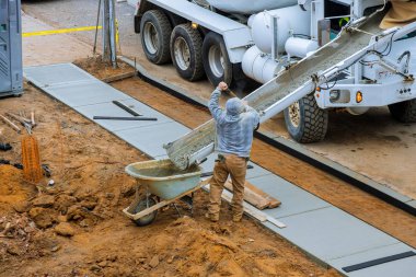 İnşaat işçisi kaldırıma çimento döktü. El arabalı karıştırıcı kamyonla beton döktü.