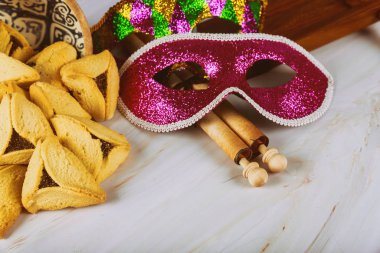 Ahşap zemin üzerinde hamantaschen kurabiyeleri, gürültü çıkarıcı ve karnaval maskesi ile geleneksel Purim